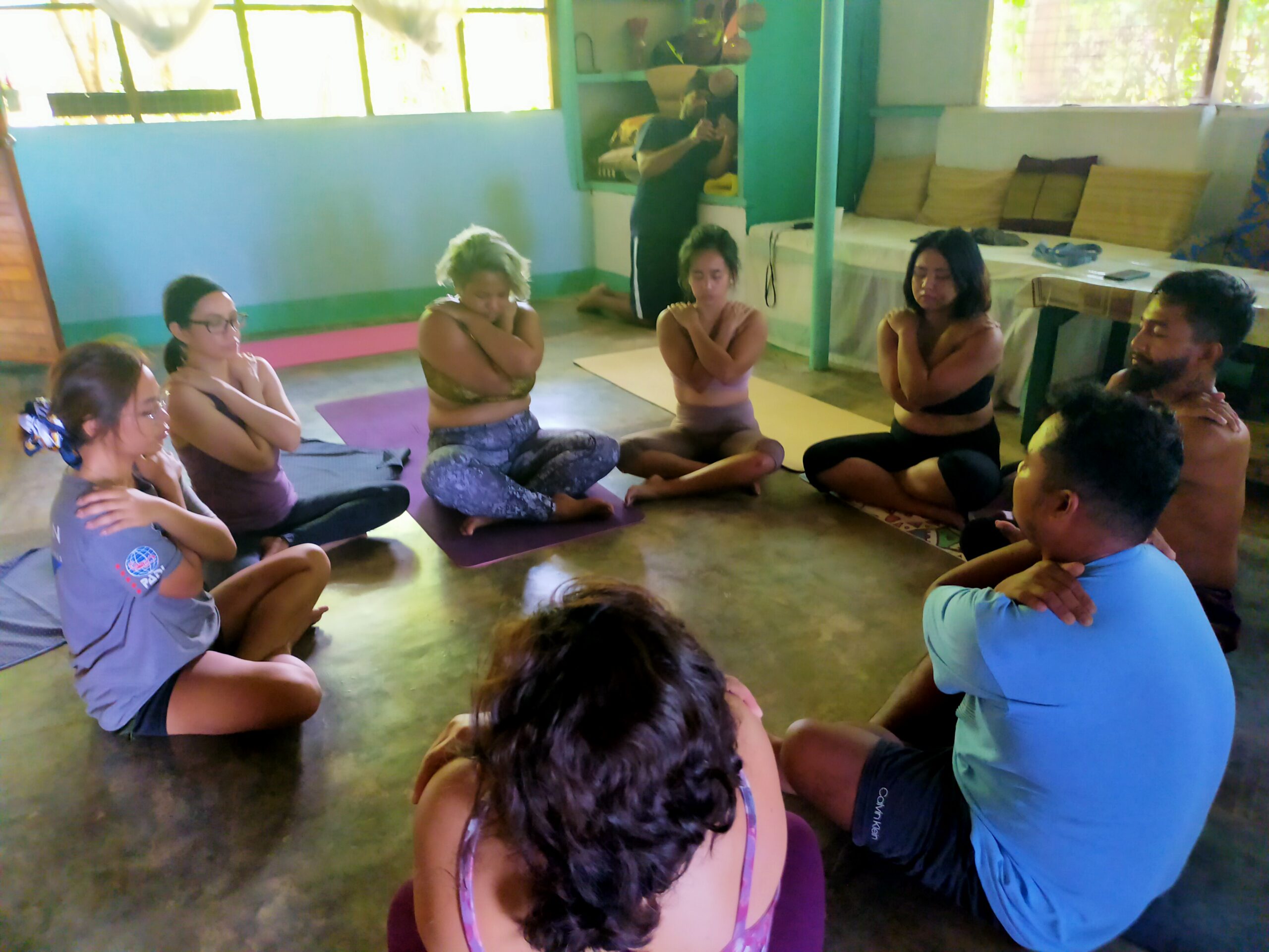 Participants engage in a mindfulness session, seated in a circle, practicing breathwork and self-hugging for relaxation and connection.